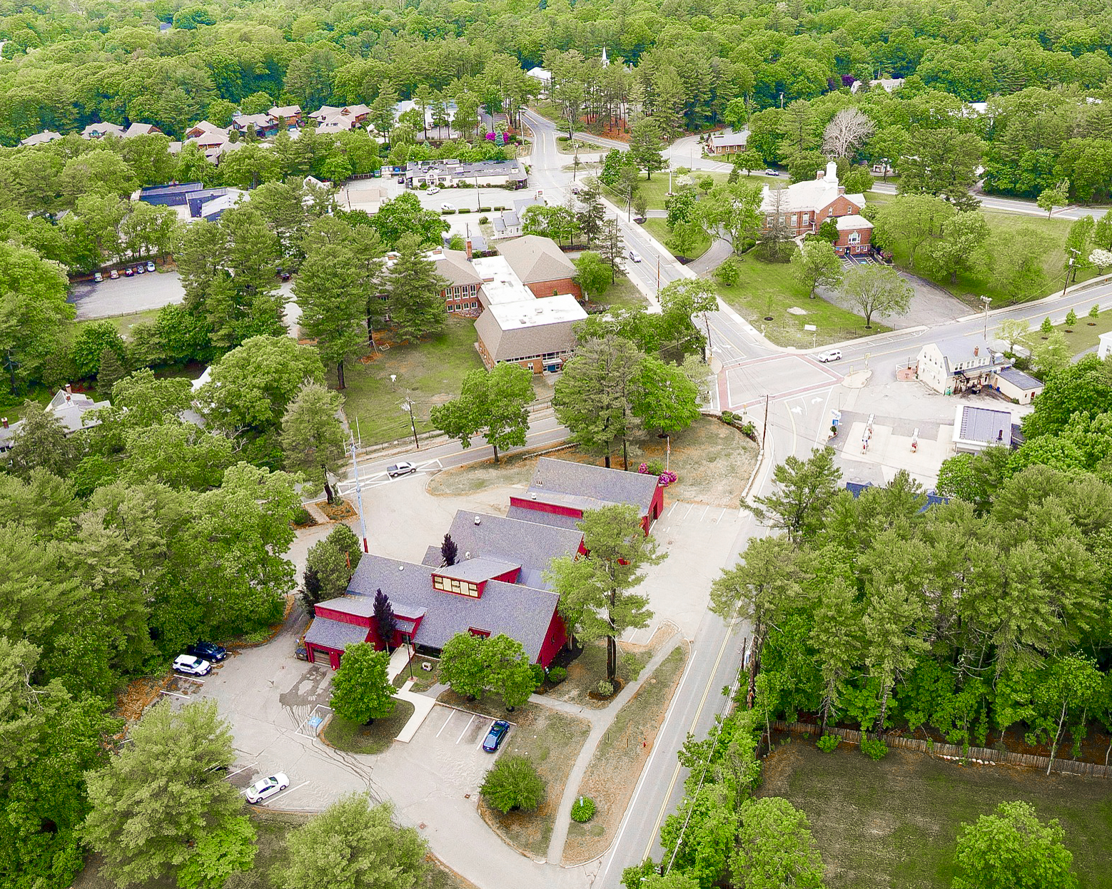 A photo shot by a drone of Dover, Massachusetts depicting a variety of 1 to 2 story buildings, roads, and lush trees